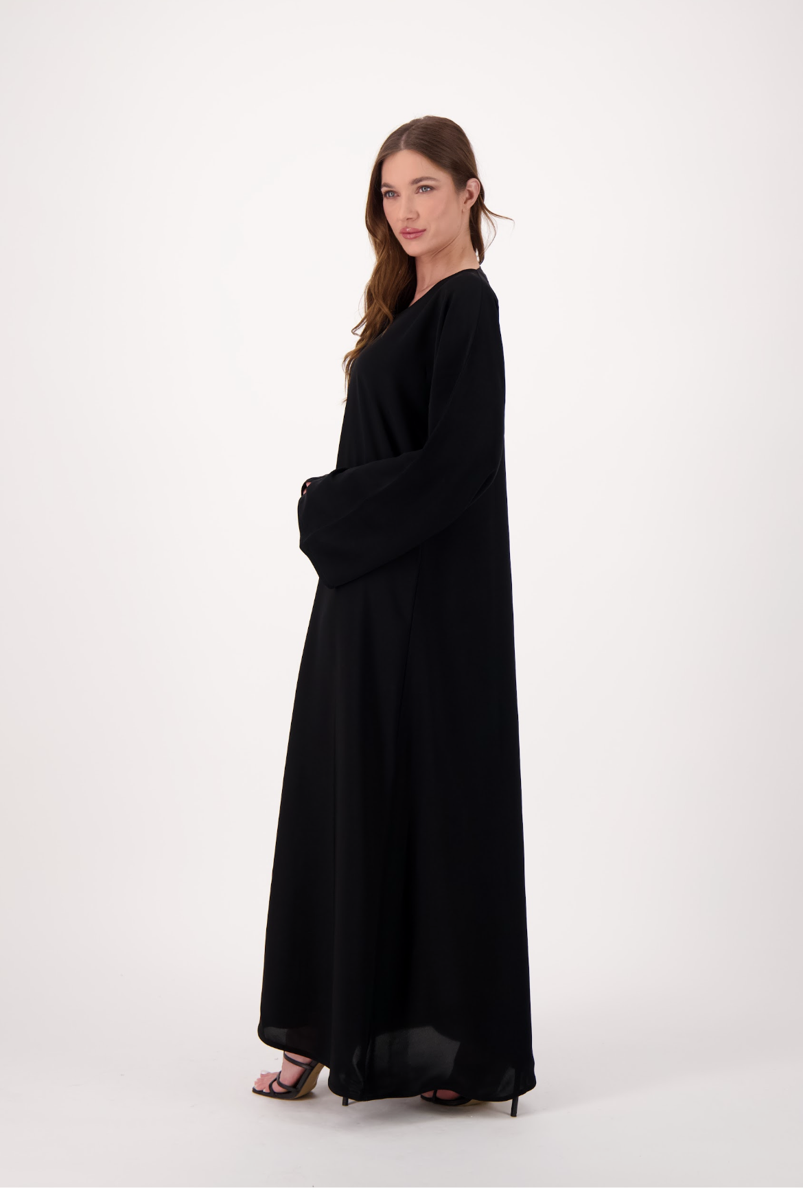 Plain black abaya made from soft, flowy Nida fabric, featuring a loose fit and full-length sleeves, worn by a model and displayed against a neutral background.